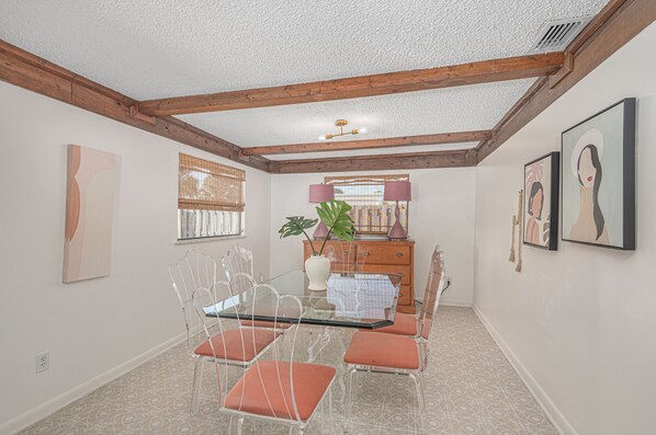A dining area with a glass table, metal chairs, a wooden ceiling, and artwork on the walls. - Pink Flamingo Island Oasis (Fort Pierce)