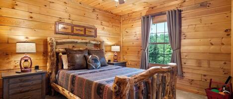 A wooden cabin bedroom with a bed, nightstands, a ceiling fan, and a window with curtains.