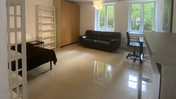 Ein geräumiger Wohnbereich mit einer schwarzen Couch, einem Holzschrank und einer weißen Trennwand.