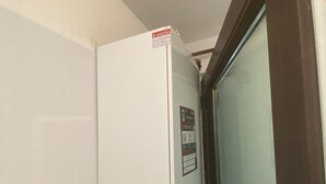 Ein weißer Durchlauferhitzer an der Wand, ein rotes Werkzeug lehnt dagegen.