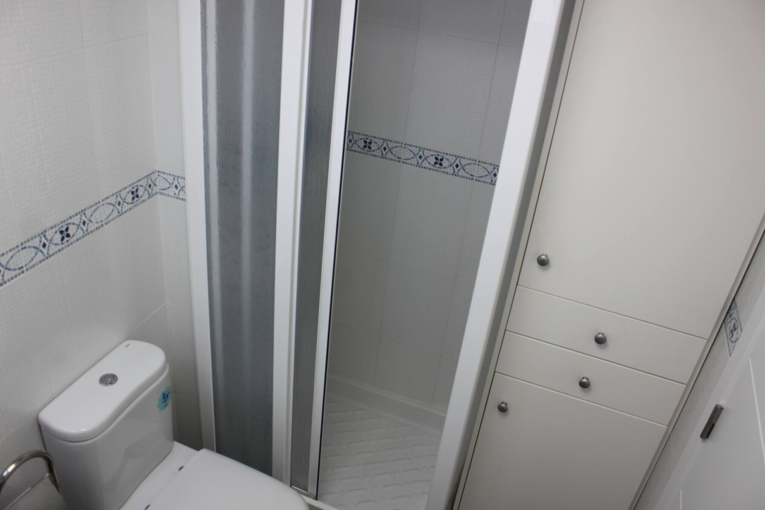 Een badkamer met toilet, douche met glazen deur en een kast met lades.