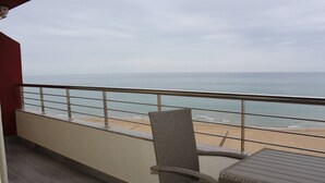 A balcony with a wicker chair and a small table, overlooking a beach with a railing. - Don Ximo 13º  Solo Familias! (Playa de Gandía)
