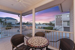 A balcony with a table and chairs, overlooking a residential area with houses and a clear sky. - 🌴Private Screened Pool Home | Walk to Ft Myers Beach | Palm Island🌴 (Fort Myers Beach)