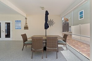 Een overdekt buitenruimte met een eettafel en stoelen, een bord met zwembadregels en een zondecoratie aan de muur.