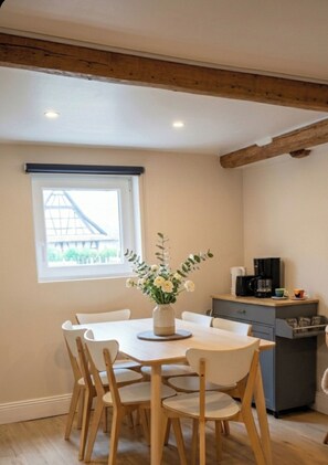 Un área de comedor con una mesa y sillas, un florero con flores, una ventana con vistas y una kitchenette.