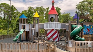 Ein Spielplatz mit mehreren Rutschen und Klettergerüsten, umgeben von einem Holzzaun und Bäumen.