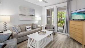 Ein modernes Wohnzimmer mit Sofa, Couchtisch und Fernseher, mit Blick auf die Küste durch die Glastür.