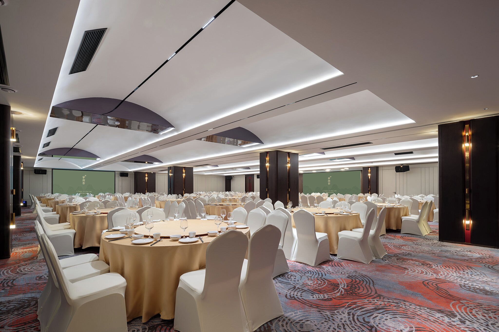A banquet hall with round tables, white chairs, and a carpeted floor.