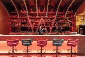 A bar with a bartender, red and blue bar stools, and shelves stocked with bottles. - voco Changsha Airport by IHG (Changsha)