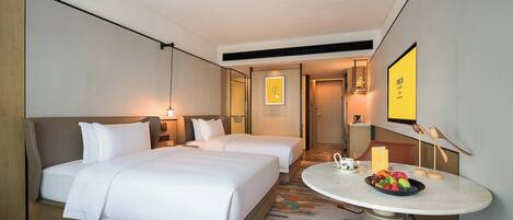 A hotel room with two beds, a round table with a fruit bowl, and a wall-mounted TV.