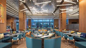 A modern restaurant with wooden paneling, teal upholstered seating, and a ceiling with reflective metallic elements.