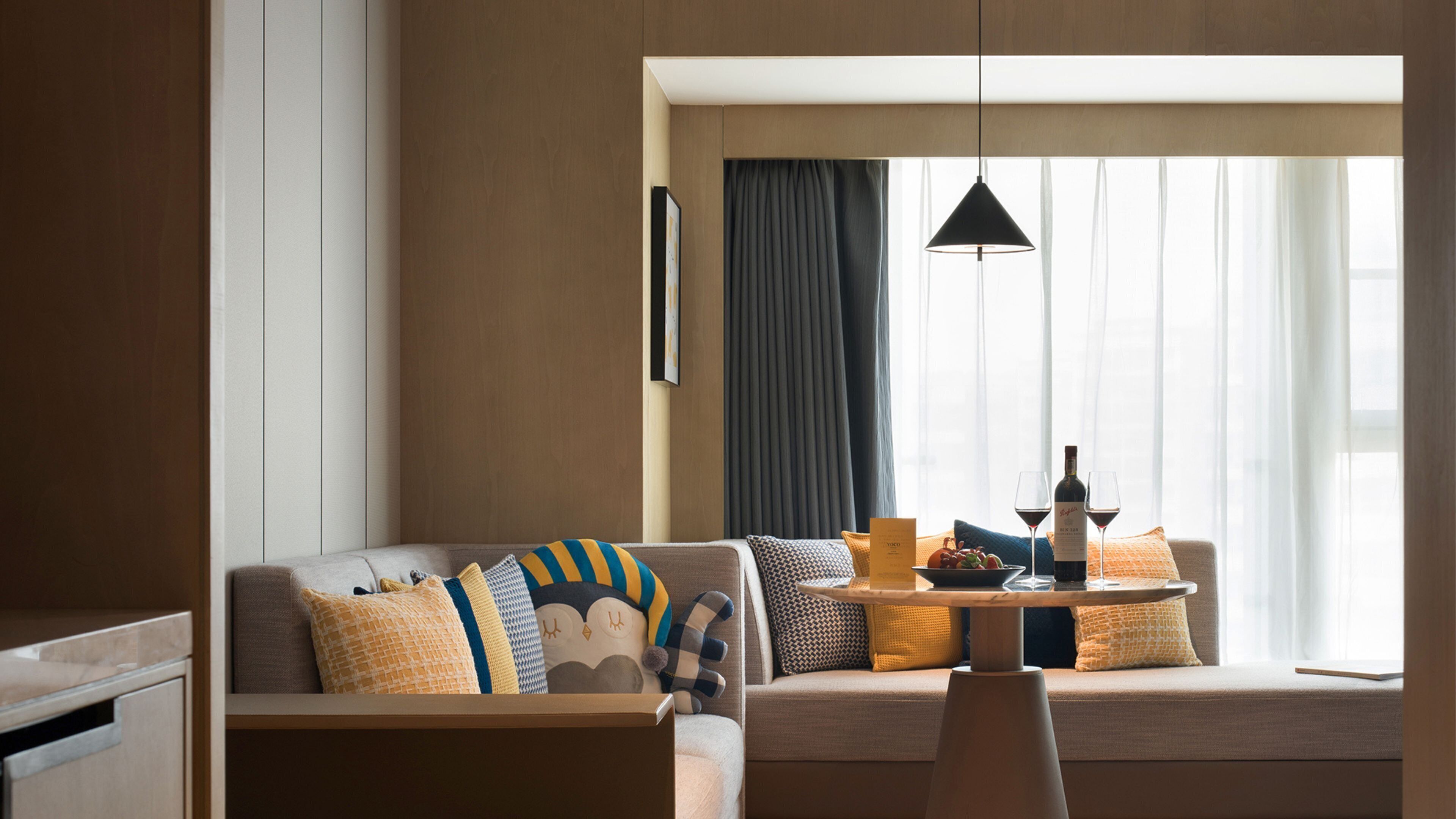 Ein modernes Hotelzimmer mit einer Couch, einem Esstisch und einem Fenster mit Vorhängen.