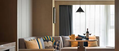 Ein modernes Hotelzimmer mit einer Couch, einem Esstisch und einem Fenster mit Vorhängen.