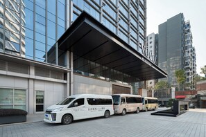 A modern building with a glass facade and a covered entrance. There are three white vans parked in front. - voco Changsha Airport by IHG (Changsha)