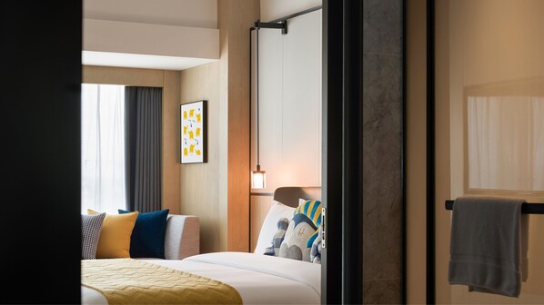 Habitación de hotel con cama, mesita de noche, lámpara colgante, ventana con cortinas y un perchero para toallas.