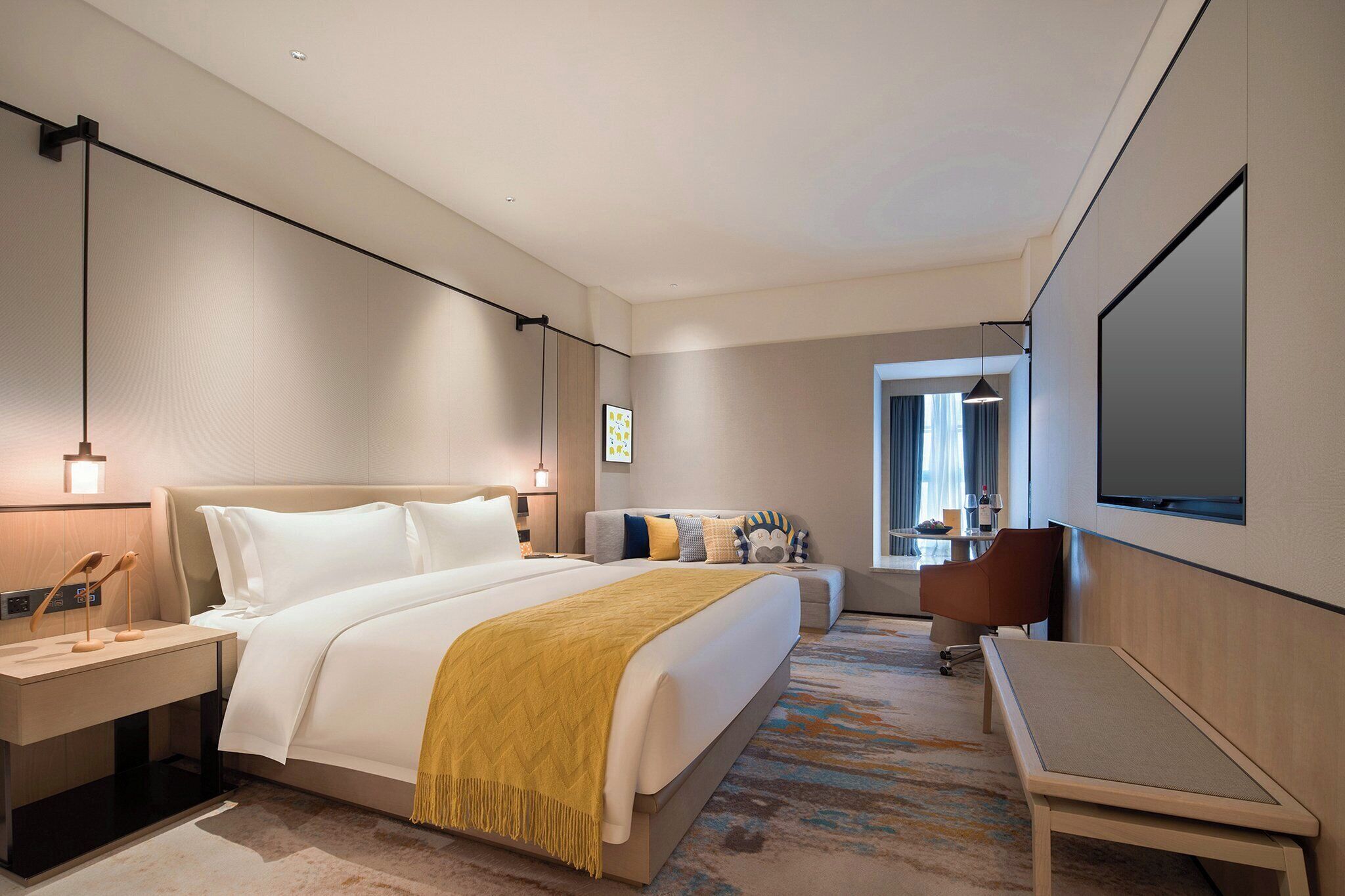 Una habitación de hotel moderna con una cama grande, un escritorio, una silla, un televisor y un ventanal con cortinas.