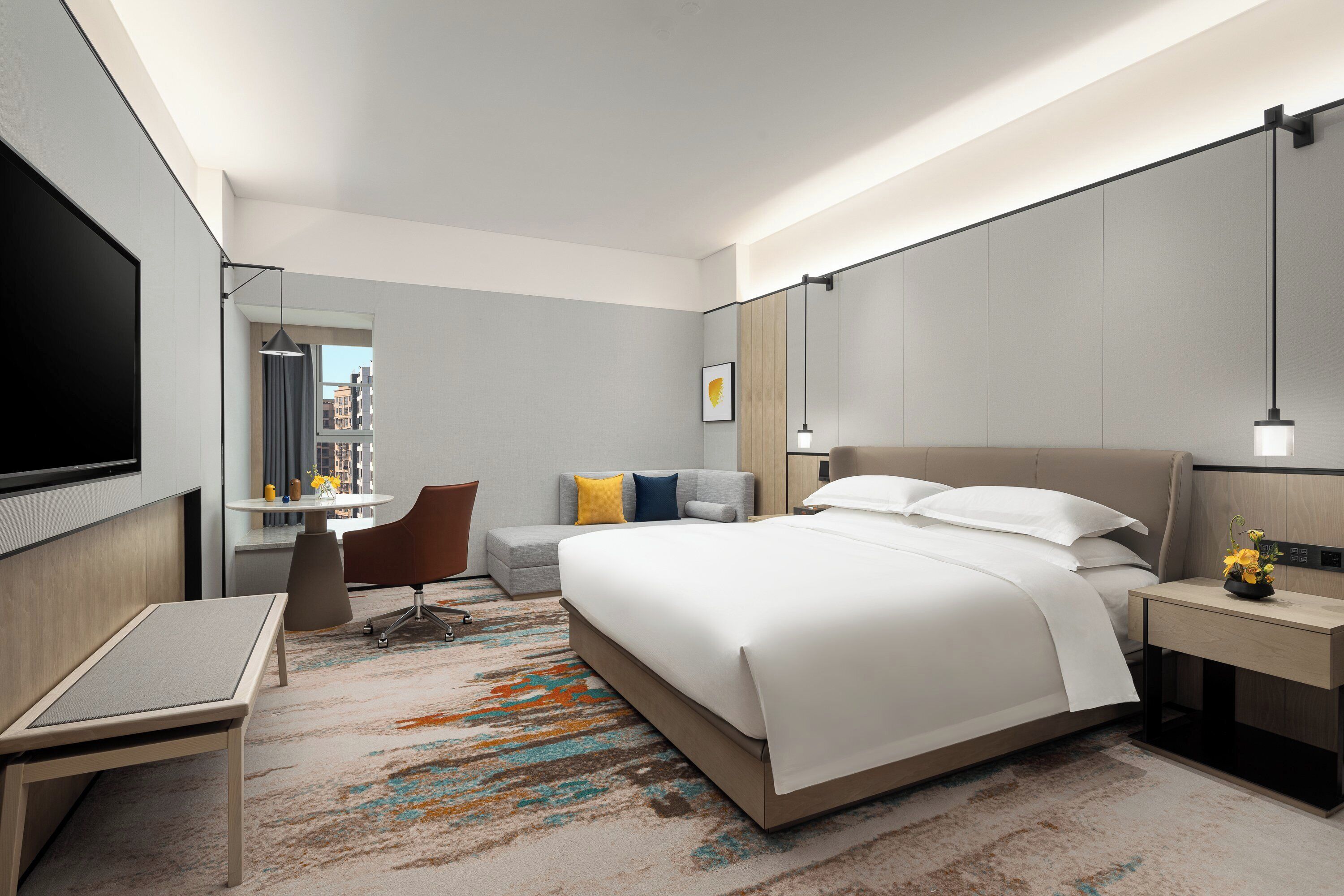 A modern hotel room with a large bed, a desk, a chair, and a TV.