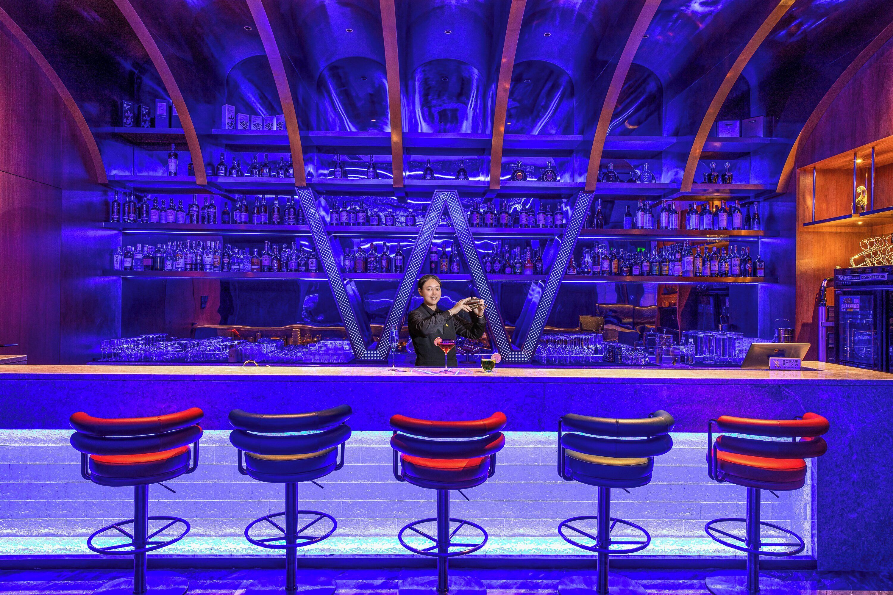 Eine Bar mit mehreren Flaschenregalen, einem Barkeeper und Barhocker.