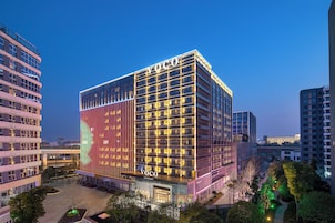 Un hotel moderno con un llamativo letrero de 'Voco', rodeado de otros edificios y un área ajardinada.