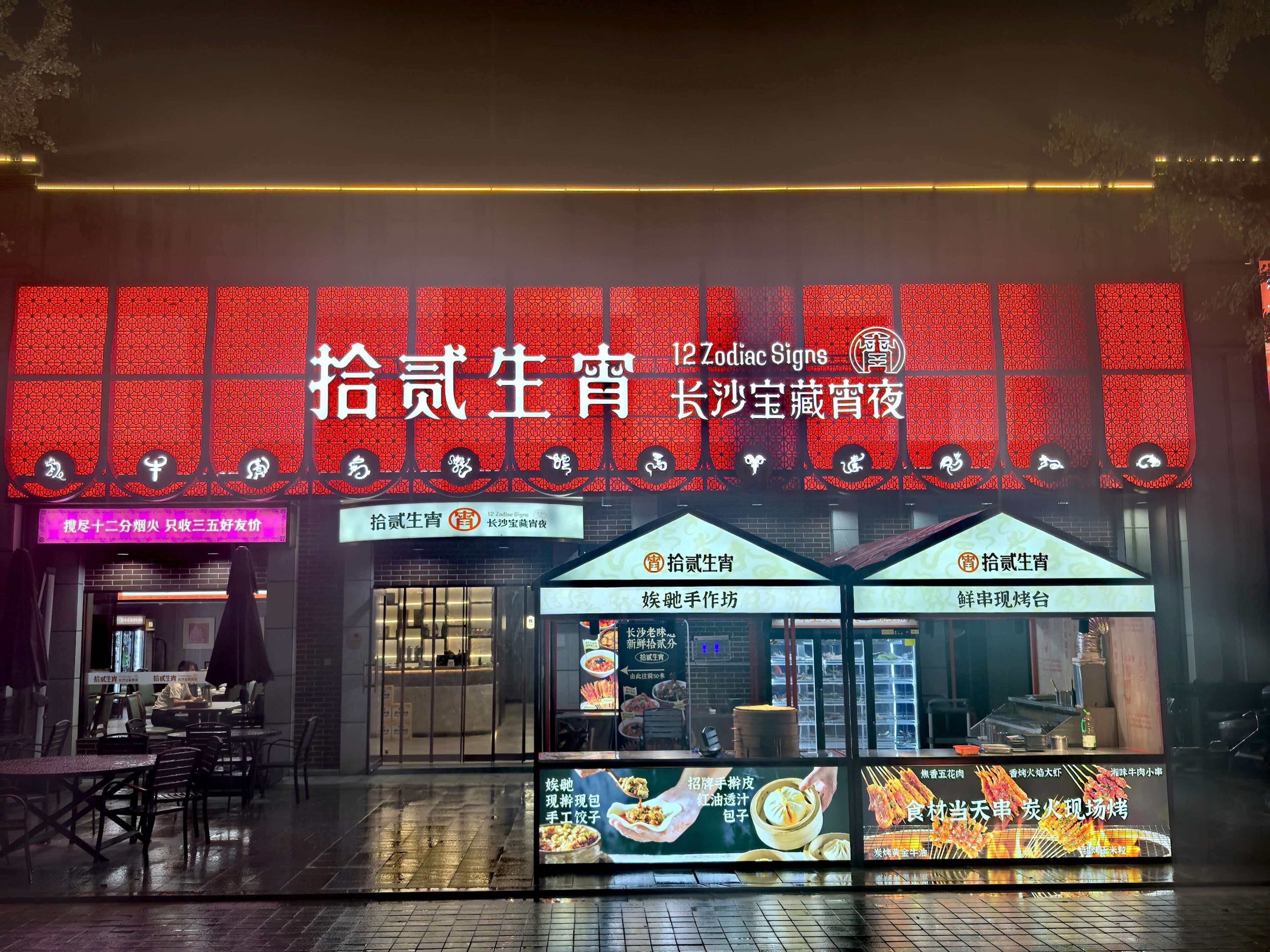 Un restaurant dont la façade est ornée d’un motif rouge et qui affiche de nombreux panneaux indiquant les différents plats et services proposés.