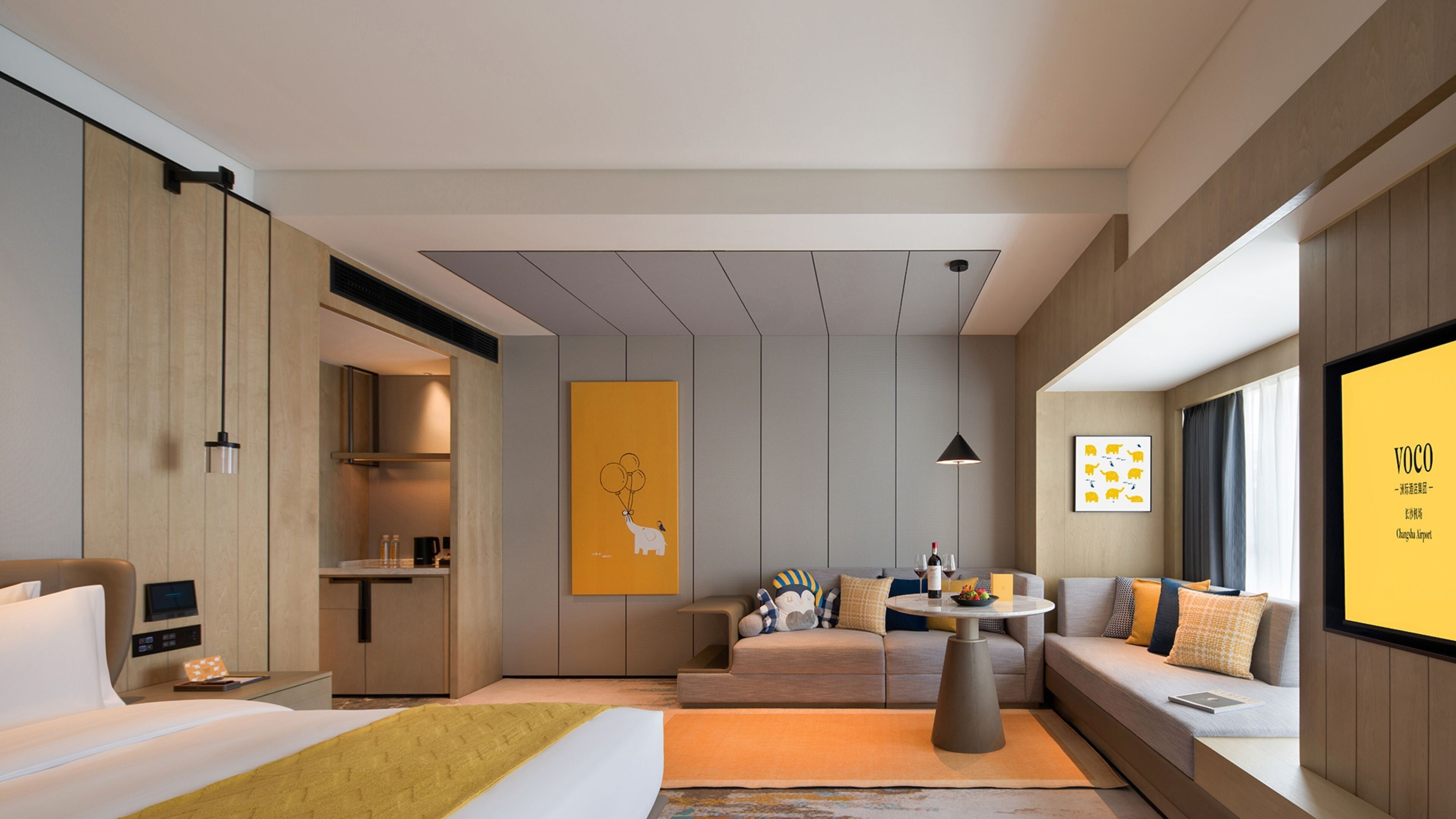 A modern hotel room with a bed, sofa, dining table, and artwork.