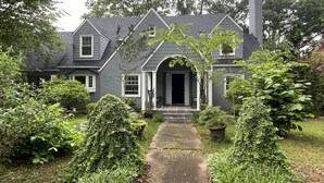 Une maison à deux étages, à l’extérieur de couleur gris foncé, avec un porche à l’avant doté d’une balustrade blanche et un chemin menant à l’entrée.