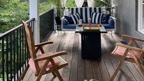 Une véranda couverte avec un plancher en bois, un ventilateur de plafond, un canapé à rayures et une table avec des chaises.