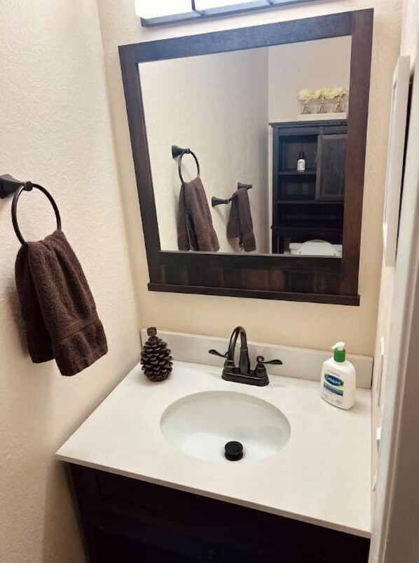 Un baño con un lavamanos blanco, un espejo de madera oscura y una toalla colgada en un perchero.