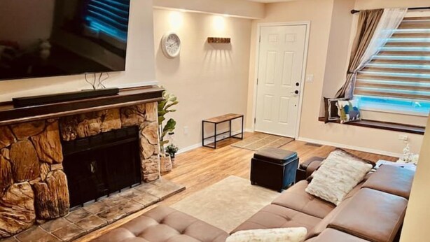 A living room with a stone fireplace, a brown leather sofa, a television, and a door. - Rustic-modern style Alaskan retreat (Anchorage)