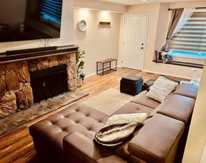 Una sala de estar con chimenea de piedra, un sofá de cuero marrón, un televisor y una puerta.
