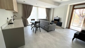 A modern living room with a sofa, a dining table, and a TV. There is a kitchen area with a kettle and a sink. -  ARCADIA OF BODRUM (Bodrum)