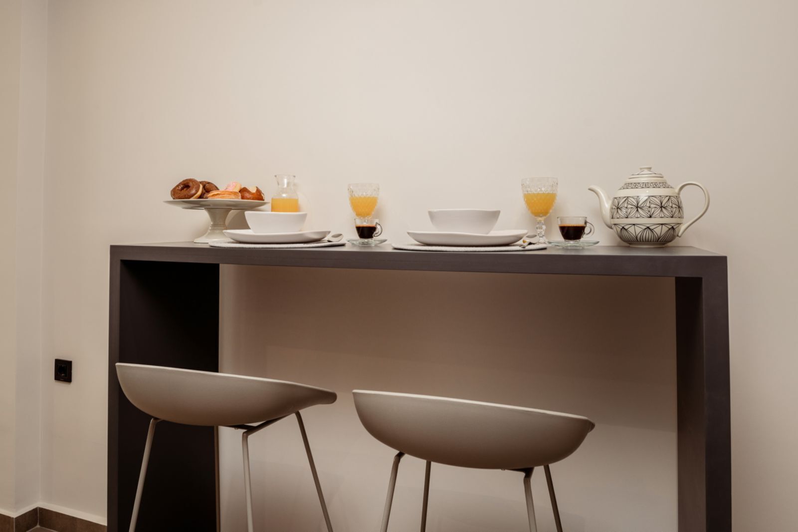 Un espace repas moderne avec une table sombre, deux chaises au design minimaliste et un pichet décoratif.