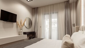 A modern hotel room with a large bed, a flat-screen TV mounted on the wall, a desk with a chair, and a window with sheer curtains. - La Maison Suite   Suite 2 (Zakynthos)