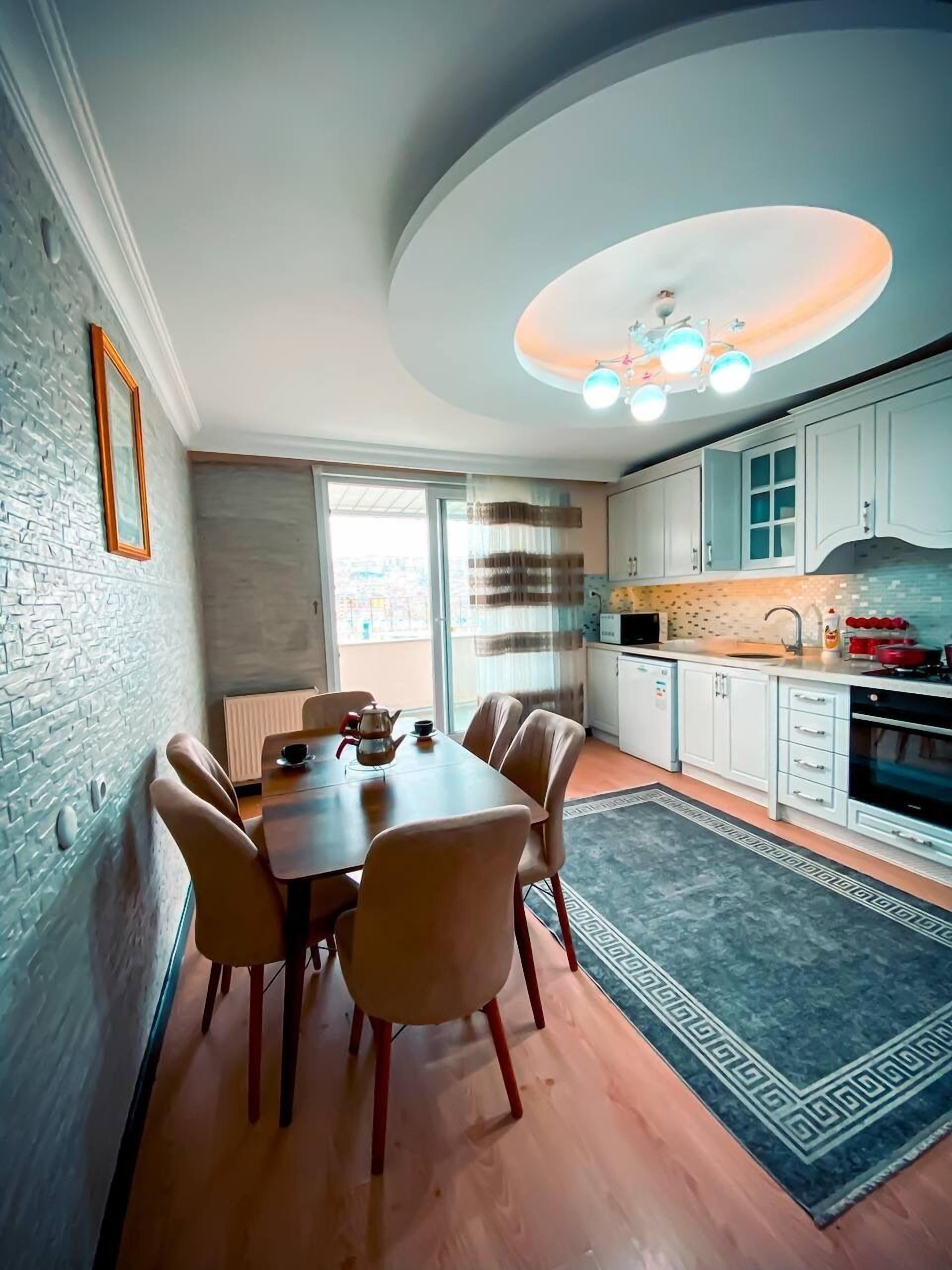 A modern kitchen with white cabinets, a dining area with a wooden table and chairs, and a patterned rug.