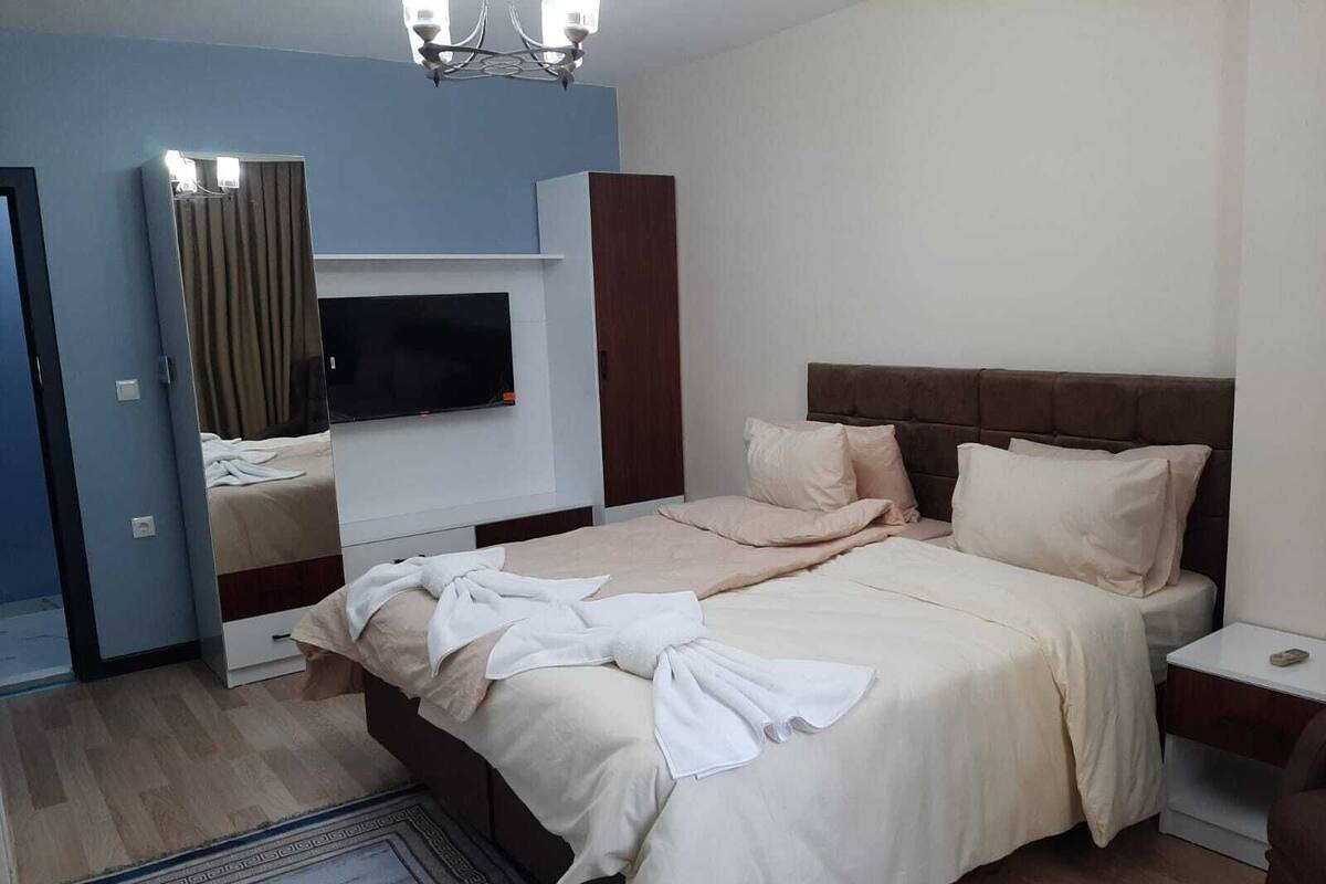 A modern hotel room with a large bed, a flat-screen TV mounted on the wall, and a wooden wardrobe.