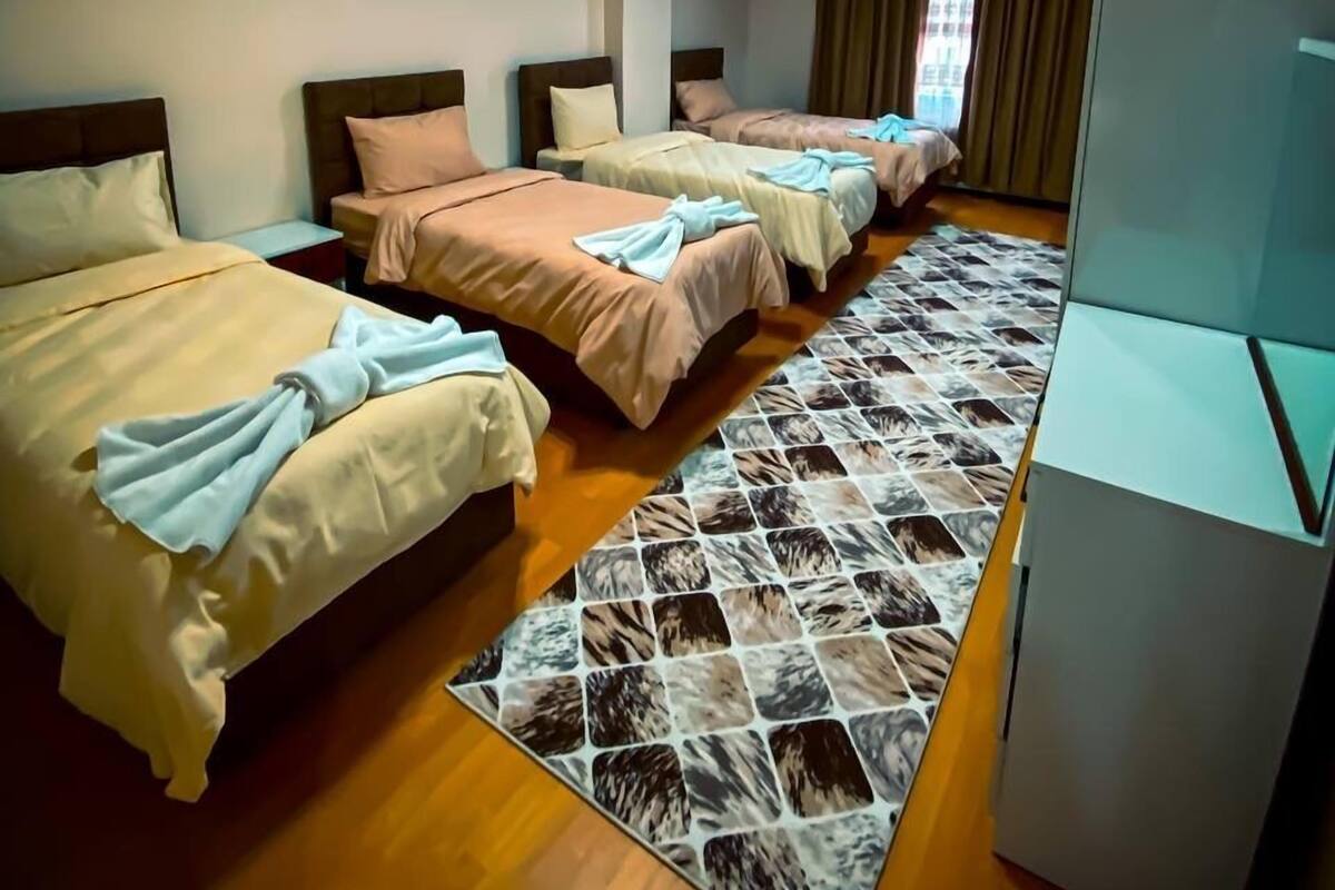 A hotel room with three beds, a large rug, and a television.