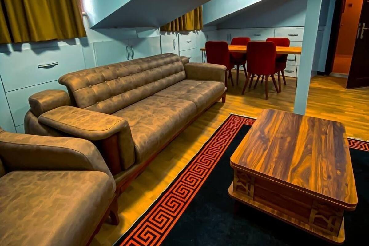 A modern living room with a sofa, coffee table, and red chairs. A kitchen area is visible in the background.