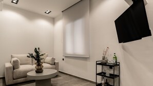 A modern, minimalist room with a beige sofa, a round coffee table, and a black shelving unit against the wall. - La Maison Suites   Studio 3 (Zakynthos)