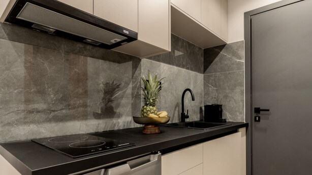 A modern kitchen with a black countertop, stainless steel appliances, and a marble backsplash. - La Maison Suites   Studio 3 (Zakynthos)