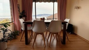 A dining area with a table and chairs, large windows with curtains, and a view of a landscape. - H Retreat   10 Min to City and 10 Min to Airport (Howrah)