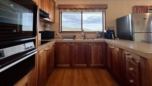 A kitchen with wooden cabinets, a black oven, a stainless steel refrigerator, and a window with a view. - H Retreat   10 Min to City and 10 Min to Airport (Howrah)