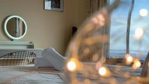 A bed with a white blanket, a round mirror on a white stand, and a window with a view. - H Retreat   10 Min to City and 10 Min to Airport (Howrah)