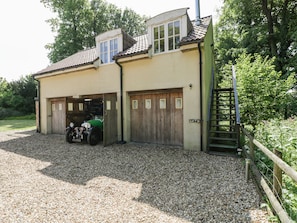 A two-story house with a gravel driveway, a green car parked in the garage, and a wooden fence.