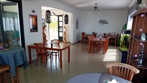 Un comedor amplio con mesas y sillas de madera, un mantel azul sobre una mesa y un ventilador de techo.
