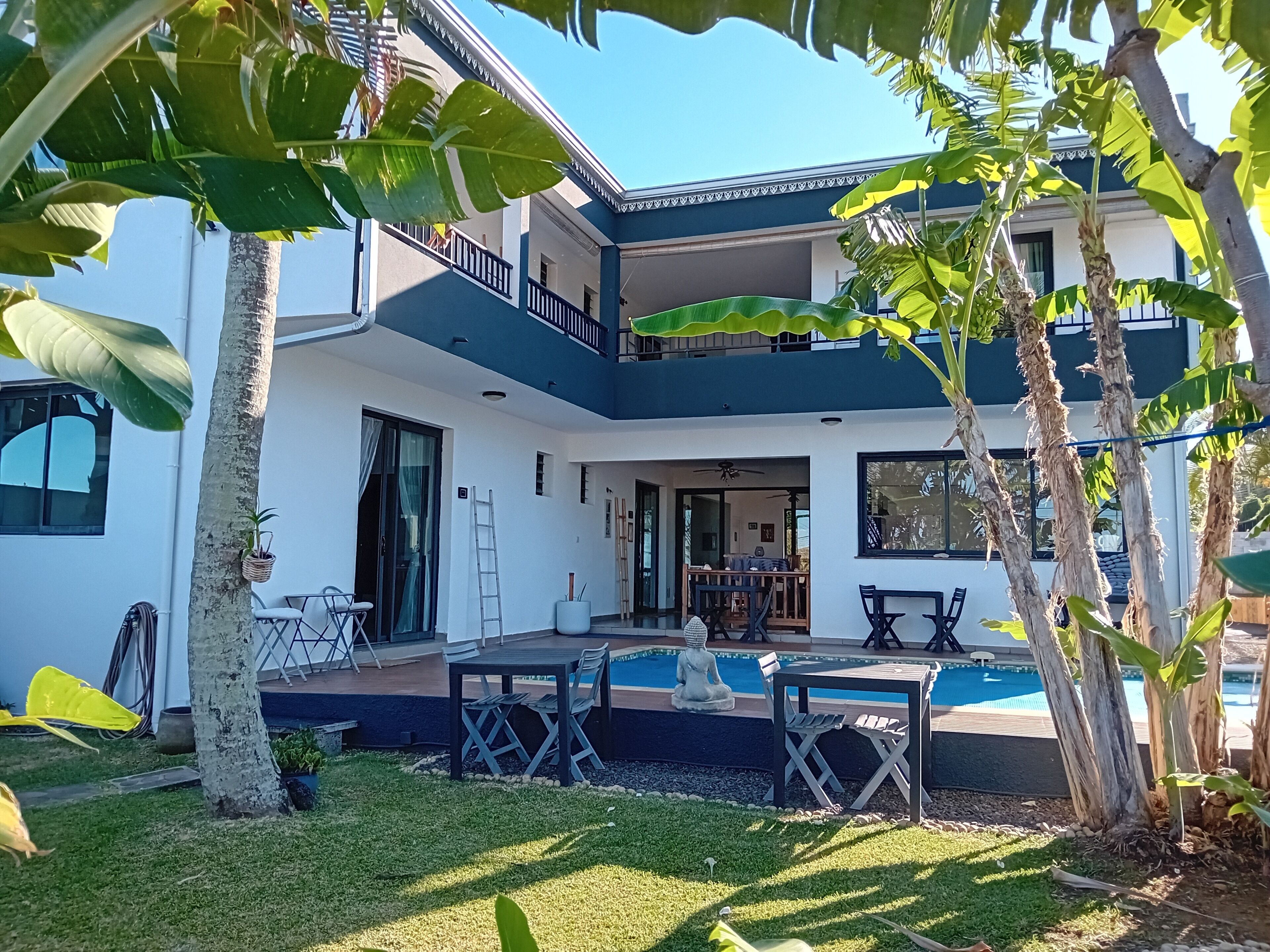 Une maison à deux étages avec une piscine, un espace salon extérieur et un balcon.