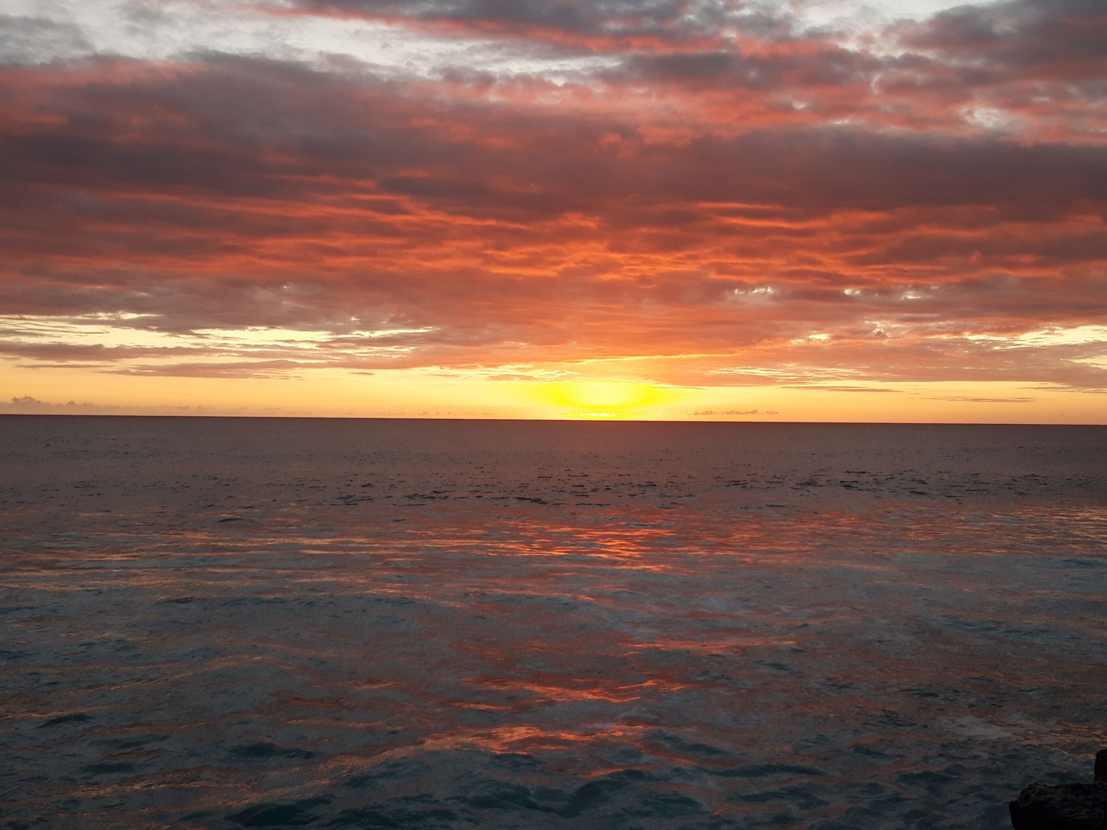 Ein Sonnenuntergang über ruhigem Meer mit klarem Horizont.