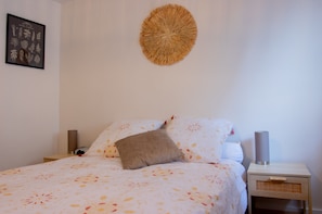 A neatly made bed with a patterned bedspread, a single brown pillow, two bedside lamps, and a framed botanical print on the wall. - Bergerie du Centre-ville (Dieppe)