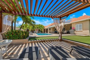 A covered outdoor area with a pool, lounge chairs, and a barbecue grill. - Private Pool Oasis 4BR Home Near Palm Beach, Aruba (Noord)