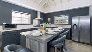 Une cuisine moderne dotée d’un grand îlot central, d’appareils électroménagers en acier inoxydable et d’un ventilateur de plafond.