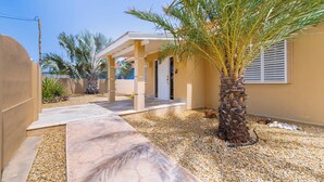 A house with a covered patio, palm trees, and a gravel driveway.